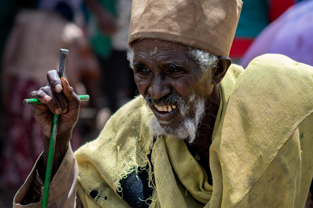 Vieil homme d'Ethiopie appuyant son regard vers l'avant et son énergie sur sa canne en forme de croix et métal vert