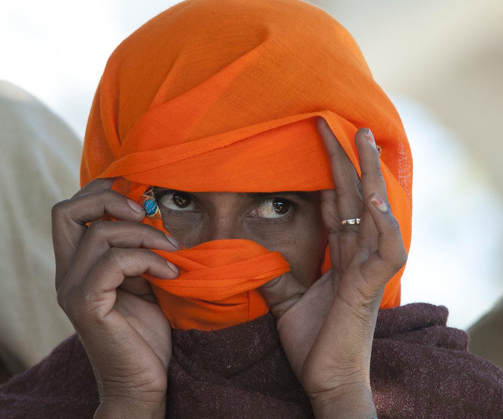 Jeune femme du Rajasthan soulevant son voile orange, broderie bleue au coin de l'oeil, pour regarder au loin